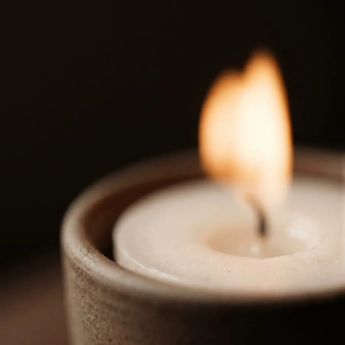 A single candle flame in a ceramic holder against a darkened room